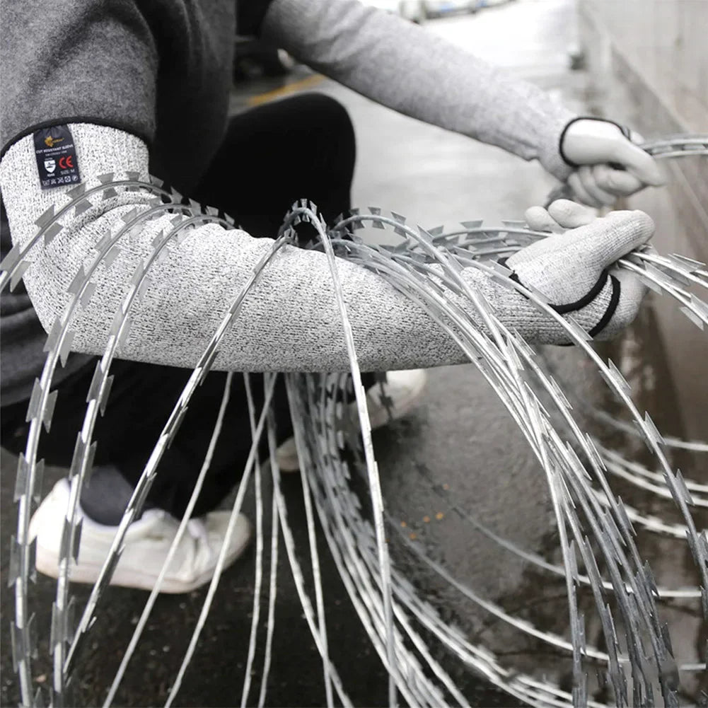 A person wearing gray arm sleeves is handling a large bundle of silver wire for protection.