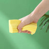A hand holds a yellow PVA absorbent cleaning sponge set against a green background.