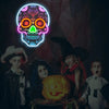 A group of children posing with a glowing neon skull sign and a carved pumpkin.