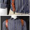 A man wearing a blue and yellow striped shirt with brown leather suspenders and light tan pants.