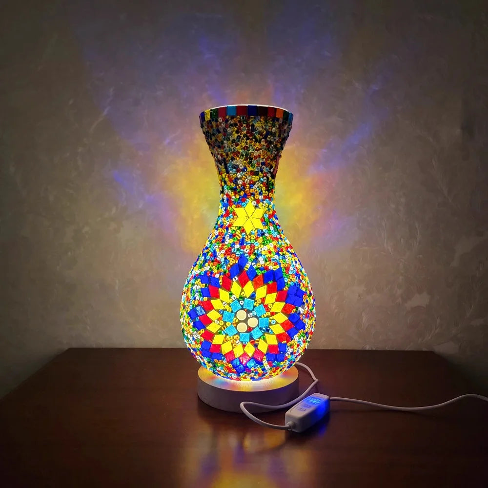 Lámpara de mesa de vidrio entrelazado y colorido con diseño de mosaico vibrante, iluminada contra un fondo oscuro.