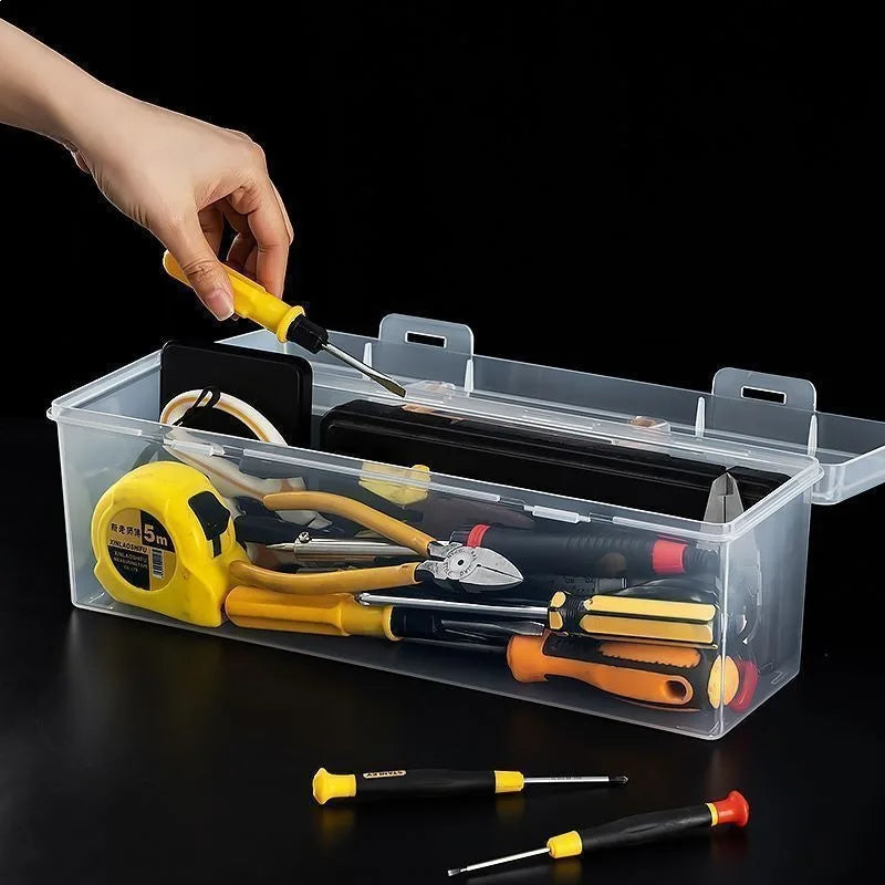 A hand places various tools, including pliers and screwdrivers, into a clear multi-compartment organizer box.