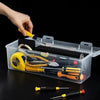 A hand places various tools, including pliers and screwdrivers, into a clear multi-compartment organizer box.