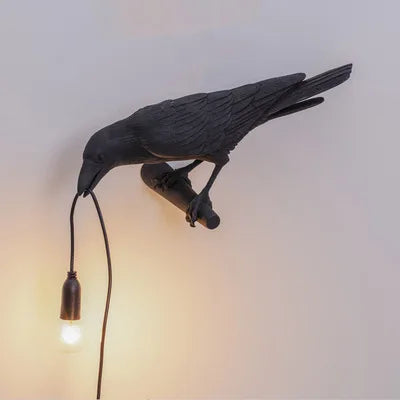 Eine dunkle Harf-Glücksvogel-Skulptur hängt an einem Schnur und beleuchtet eine moderne Tischlampe.