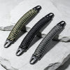 Nahaufnahme eines strapazierfähigen Paracord-Tragegurts mit Metallhaken, diagonal auf einem hellgrauen Stein.