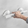 An elderly hand is using a white suction cup grab bar mounted on a tiled wall.