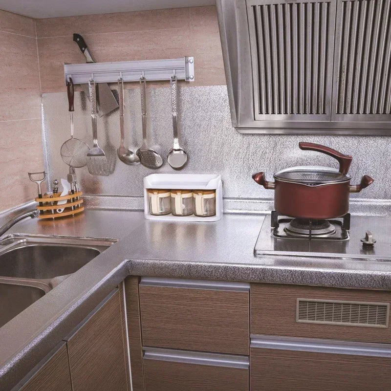 Un comptoir de cuisine montre des autocollants en aluminium sur un porte-serviette et une casserole en cuivre sur une cuisini