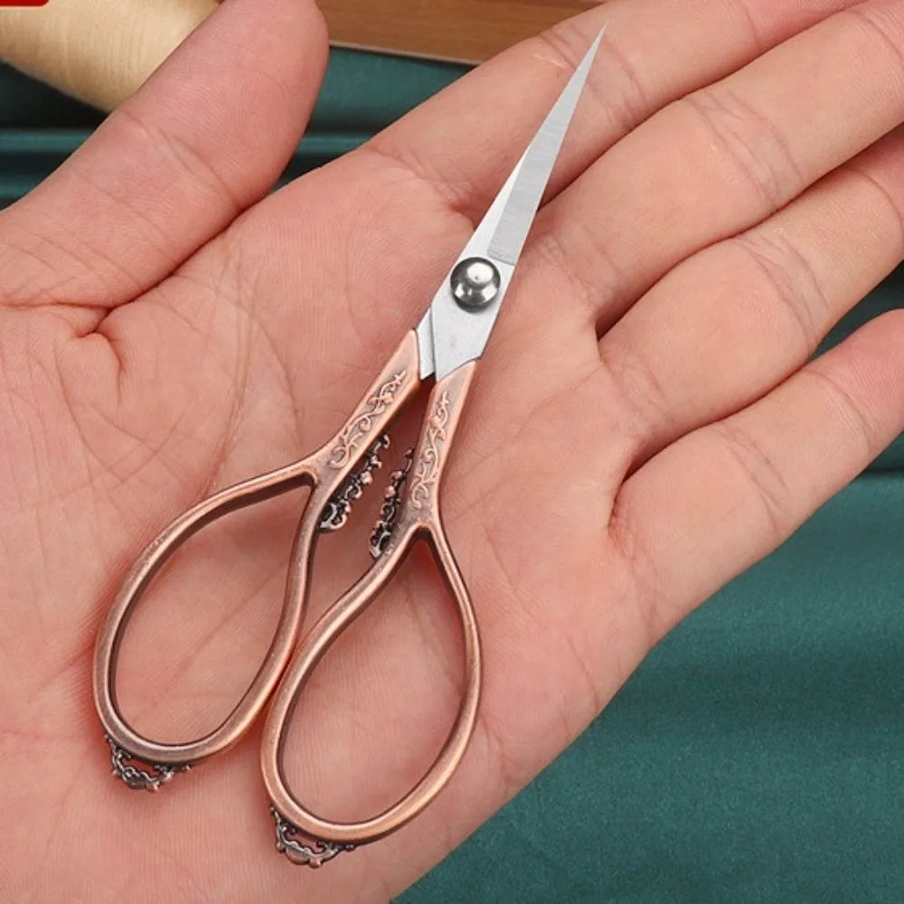 Un par de tijeras de detalle profesionales de acero inoxidable con detalles en oro rosa, sostenidas en la mano de una persona