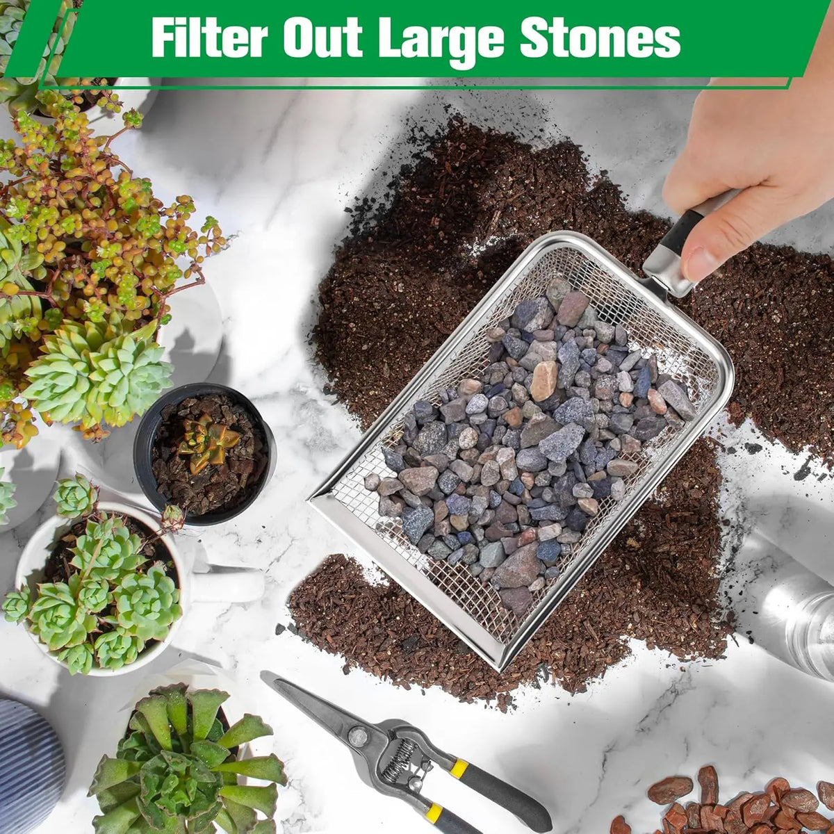 A hand is using a heavy duty stainless steel soil sieve to filter out large stones from dark soil.