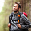 A man wearing a gray jacket and backpack is looking up, holding a handheld metal detector with pinpointing technology.