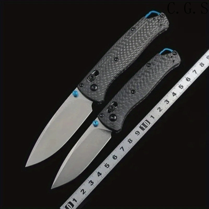 A pair of carbon fiber folding knives displayed next to a ruler for scale.