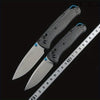 A pair of carbon fiber folding knives displayed next to a ruler for scale.