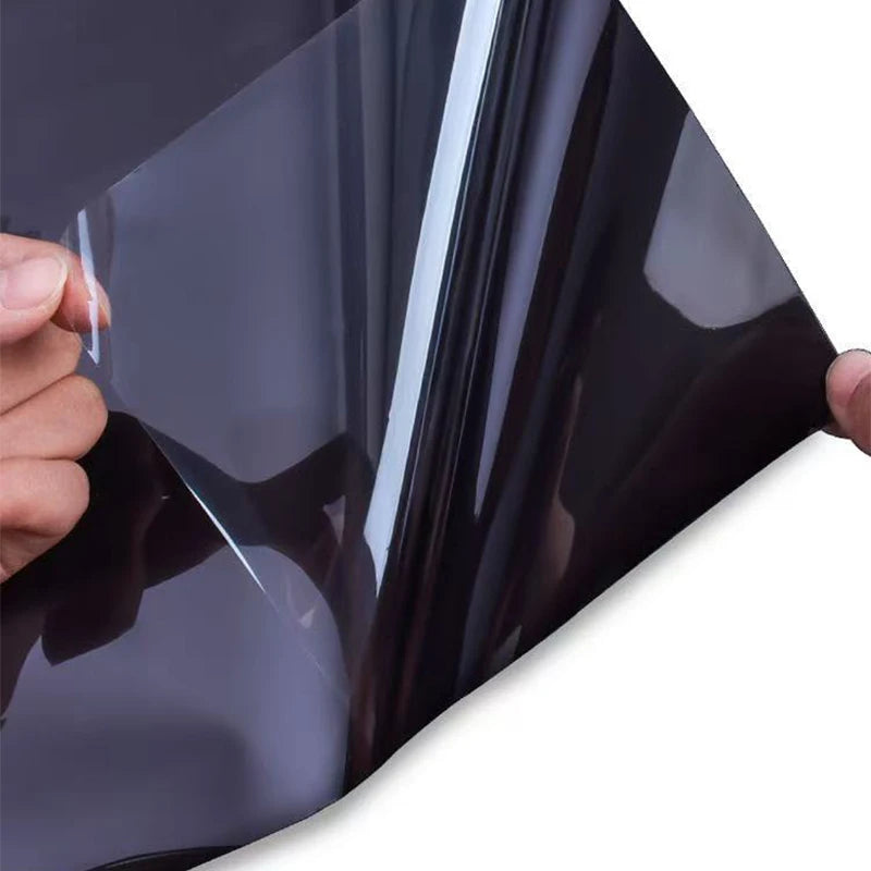 Hand applying black opaque self-adhesive window film to a glass surface for privacy and protection.