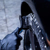 A hand is using a black detailing brush on a tire or wheel, showing the texture of the cleaning tool.