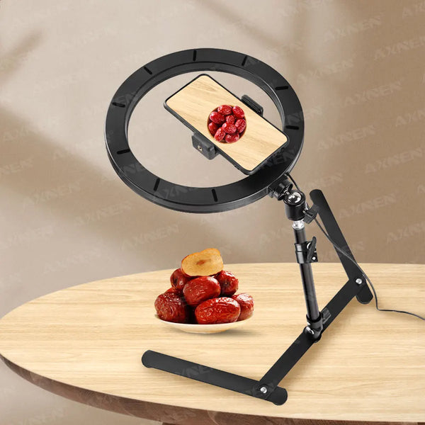 A black desktop foldable ring light mounted on a tripod, positioned above a small pile of red berries.
