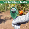 A hand holds a green soil moisture meter device in a garden setting.