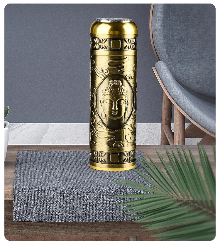 A gold-colored mini electric shaver with a Buddha design rests on a gray textured mat on a wooden surface.