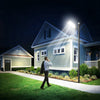 A person stands outside a house at night, adjusting an outdoor solar motion sensor LED light.