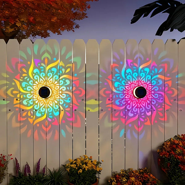 A wooden fence features colorful, glowing solar mandalas illuminating the garden area.