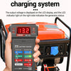 Eine Hand hält ein digitales Autobatterietestergerät, das an eine orange Generator-Einheit angeschlossen ist.