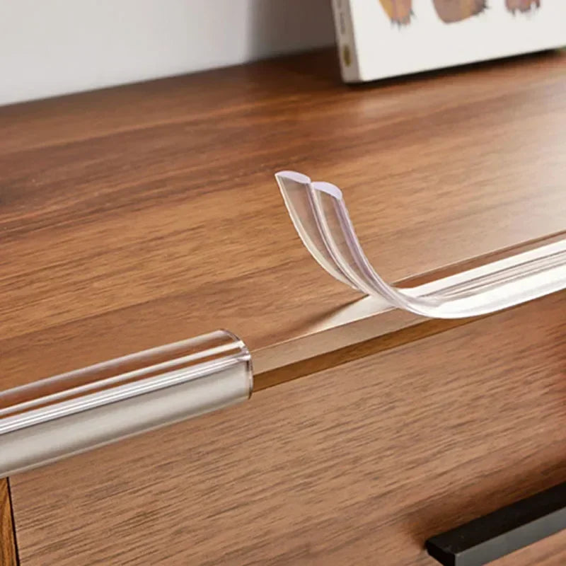 A transparent PVC baby safety edge guard is shown resting on a wooden surface.