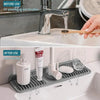 A foldable silicone sink splash mat is shown being used to direct water flow into a sink.
