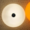 Weiße dekorative LED-Wandleuchte mit schwarzem Donut-Design vor gewebtem Hintergrund und orangefarbener Lichtquelle