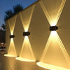 Eine Wand aus Außensolarleuchten, die eine strukturierte Wand mit nach oben gerichteten Lichtstrahlen bei Dämmerung beleuchte