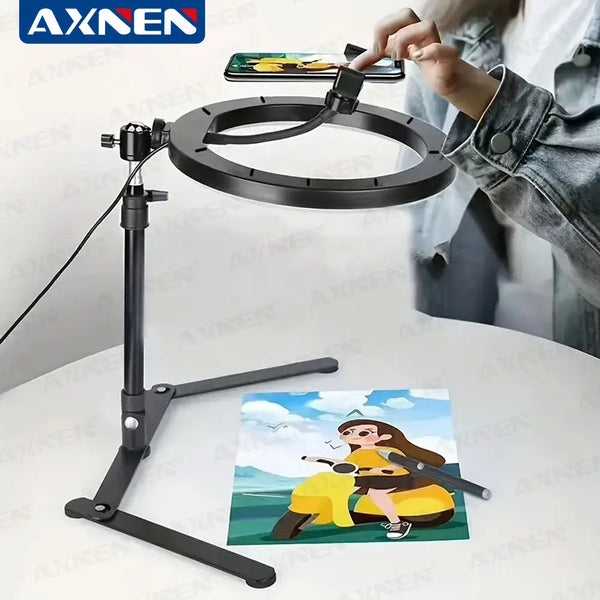A black desktop foldable ring light tripod is set up, illuminating a smartphone for photography.