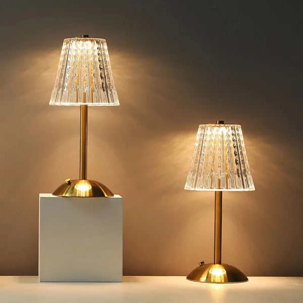 A modern table lamp with a clear textured glass shade and brass base illuminating a white surface.