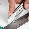 Une main utilise un cutter pour mesurer une feuille de papier blanc sur un tapis de coupe vert.