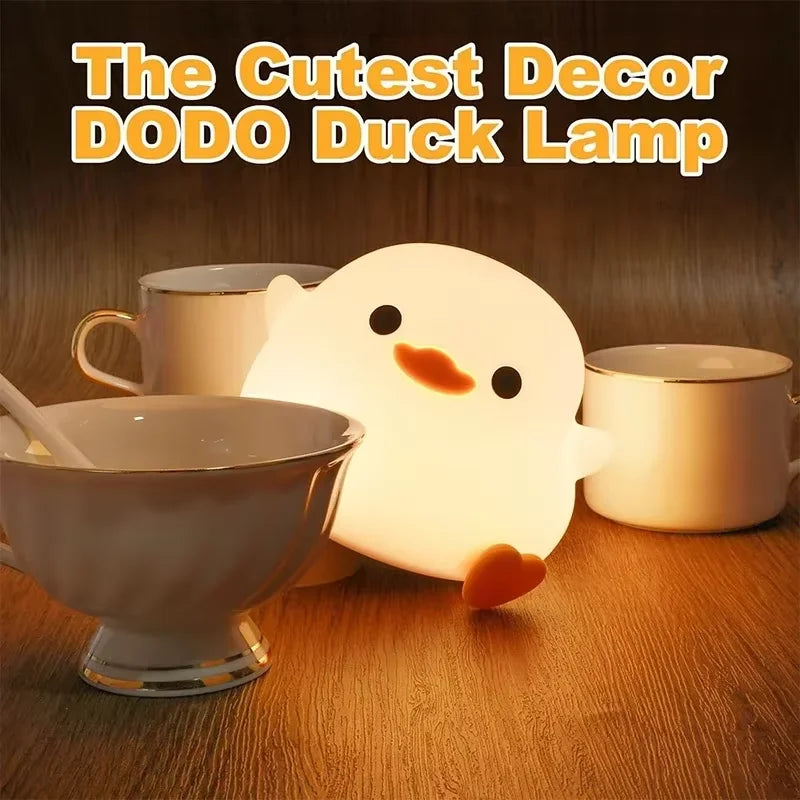 Leuchtende weiße Silikon-Entenlampe auf Holzoberfläche neben zwei Tassen.