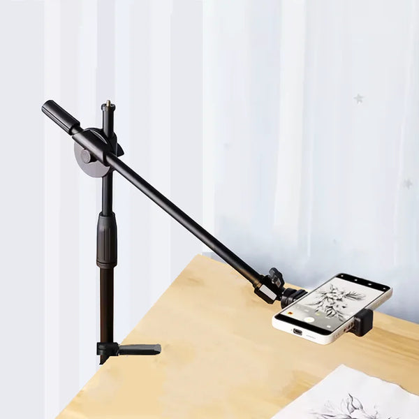 A black versatile overhead tripod with a boom arm and ring light positioned on a wooden surface.
