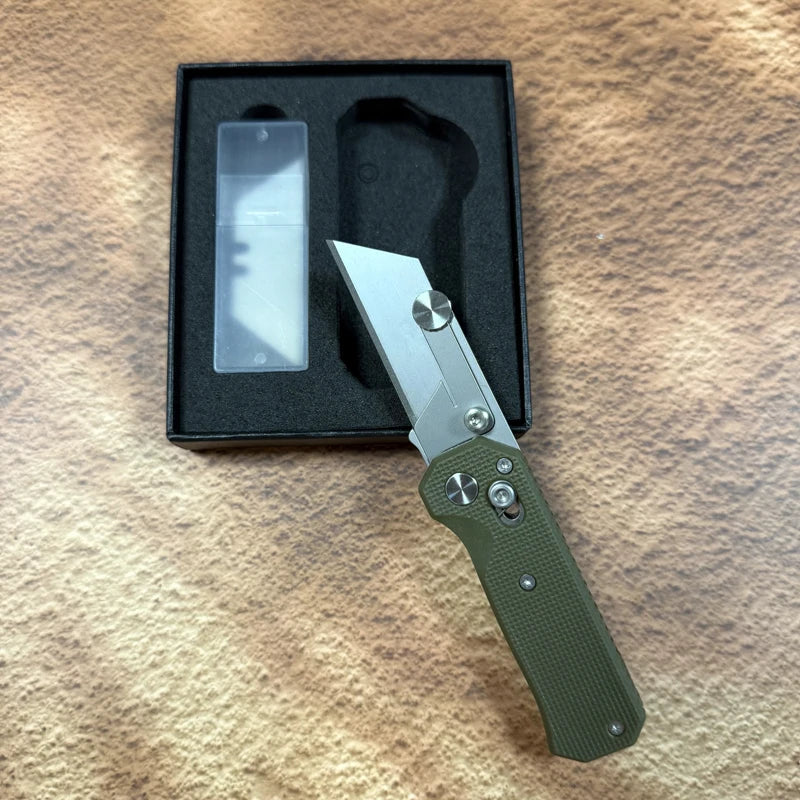 A folding utility knife with a stainless steel blade is displayed in a black box on a brown surface.