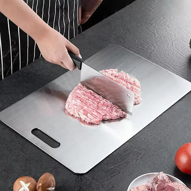 Una mano corta carne cruda en una tabla de cortar de acero inoxidable, mostrando la textura del músculo rosado.