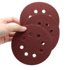 A hand holds several reddish-brown hook and loop sanding discs for orbital sanders.