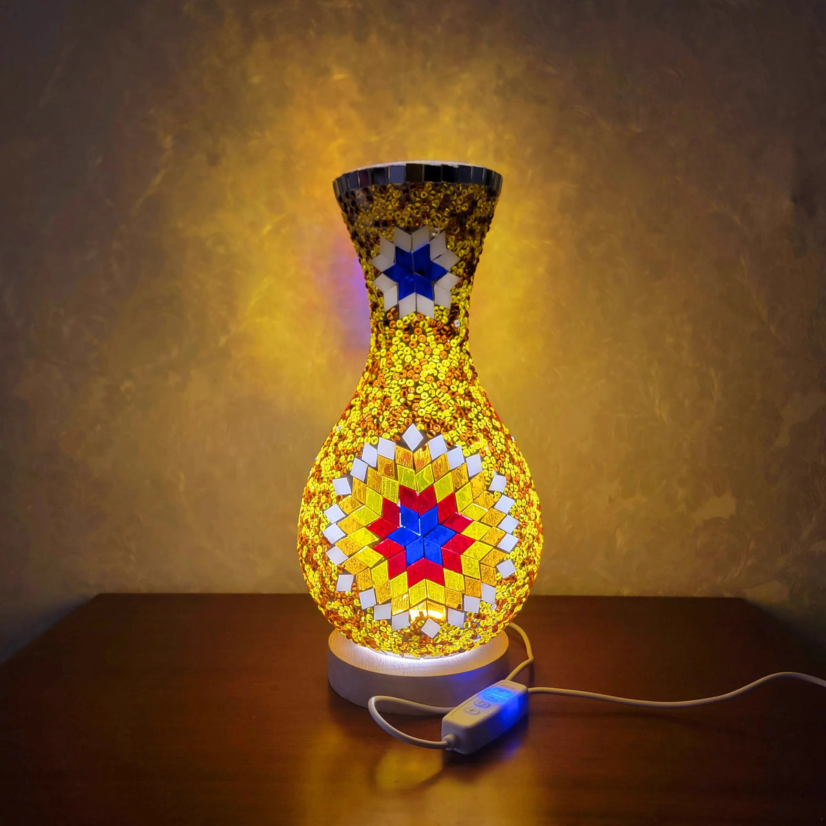 Lámpara de mesa de vidrio decorativa con base facetada dorada y brillo amarillo estampado sobre una superficie de madera.