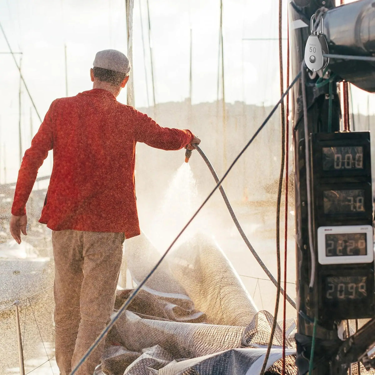 A person in a red jacket is operating a stainless steel wire rope pulley block for lifting or rigging.