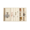 A light beige velvet jewelry storage tray with multiple compartments holding various silver and gold-toned jewelry pieces.