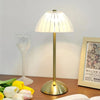 A brass table lamp with a translucent dome shade sits on a wooden surface next to a wine glass and an open book.