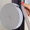 A roll of gray foam window sealing strips is shown being applied to a dark window frame.