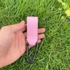 Une main tient une sangle en cuir rose avec un crochet, utilisée pour accessoires de poussette ou de sac à langer.