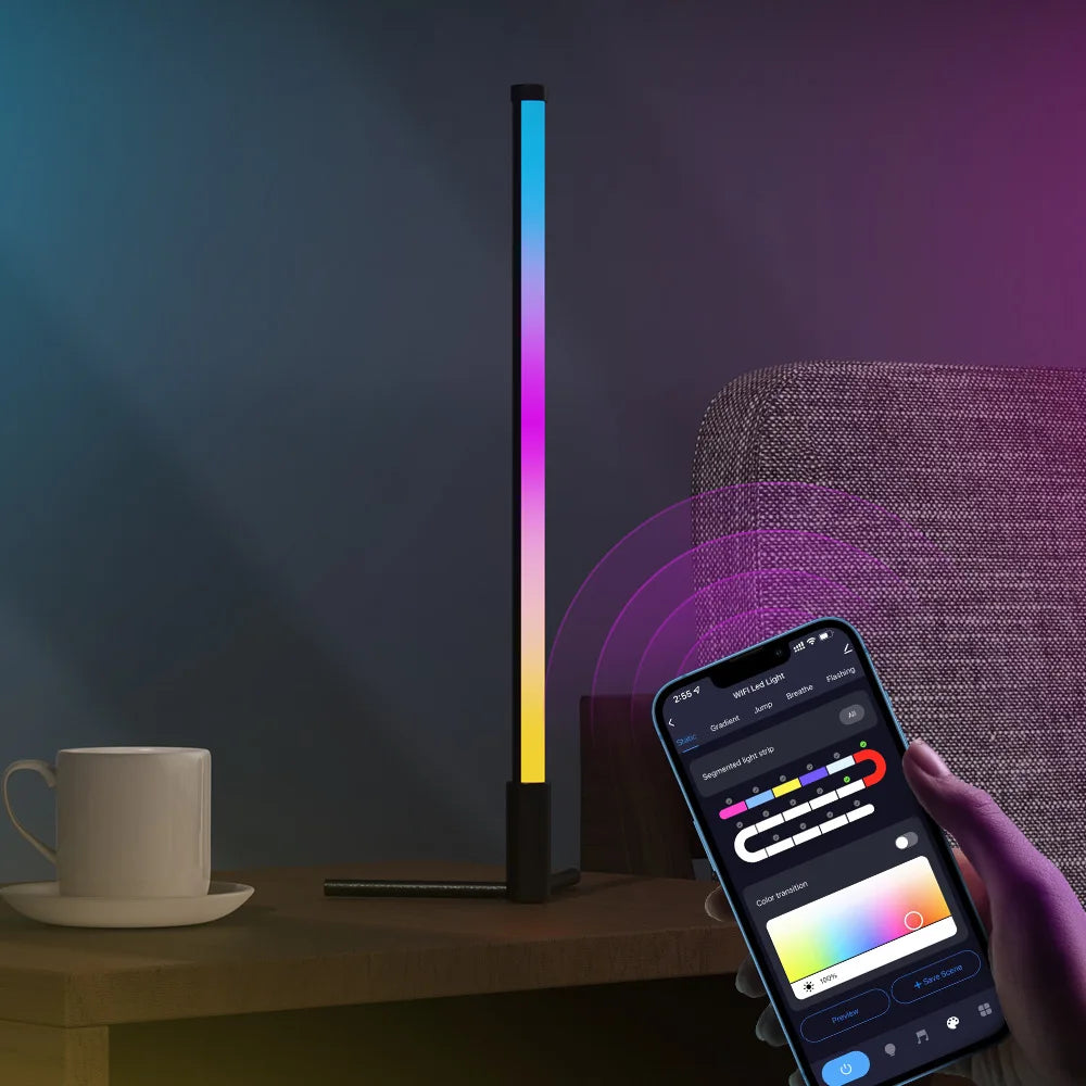 Une main tient un smartphone affichant une interface d'application à côté d'une lampe de sol verticale et élancée à LED RGB i