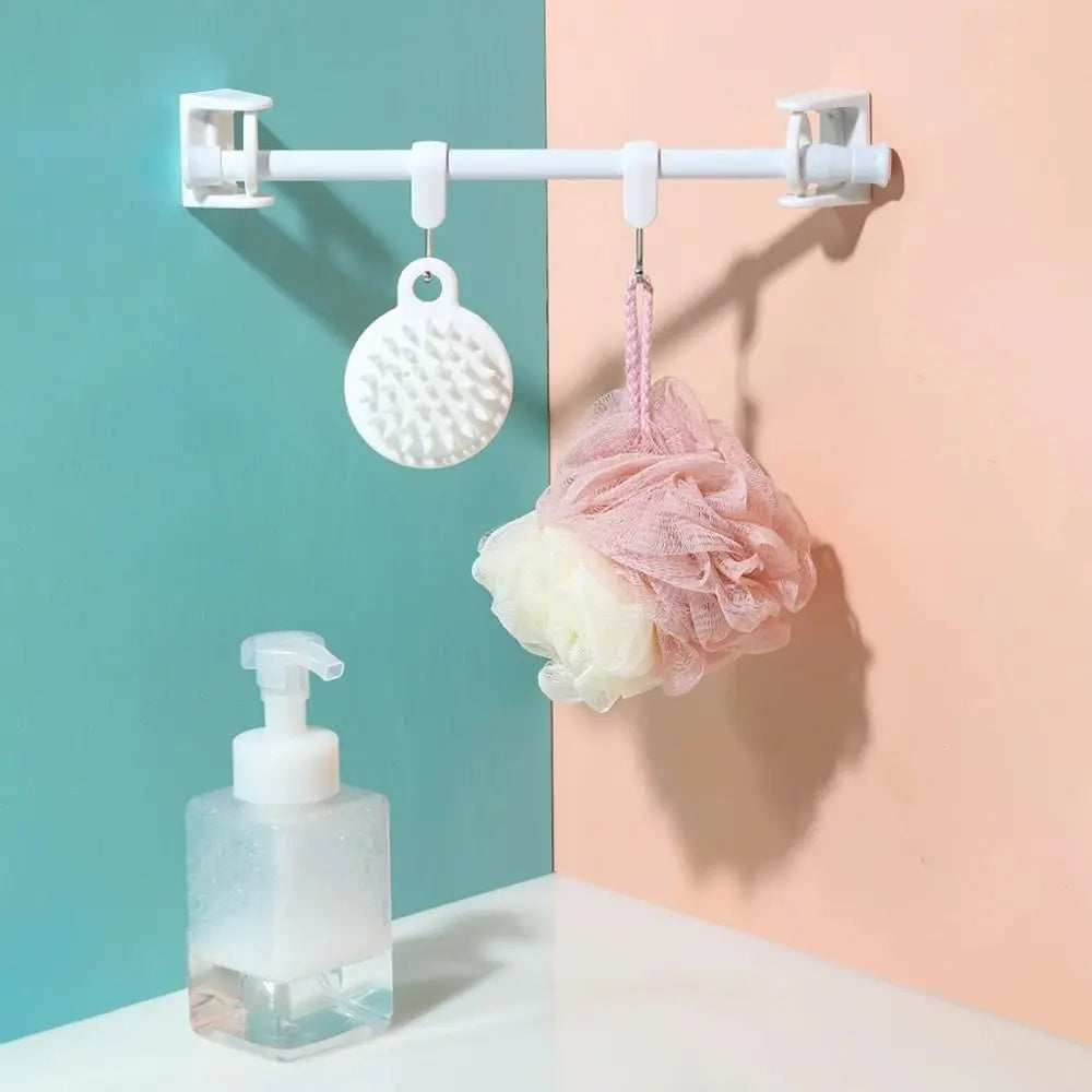 A white curtain rod with hanging brackets holds a pink and white fluffy fabric item against a light peach wall.