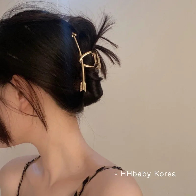 A close-up of a woman's dark hair styled in an updo with elegant gold S-shaped metal hair clips.