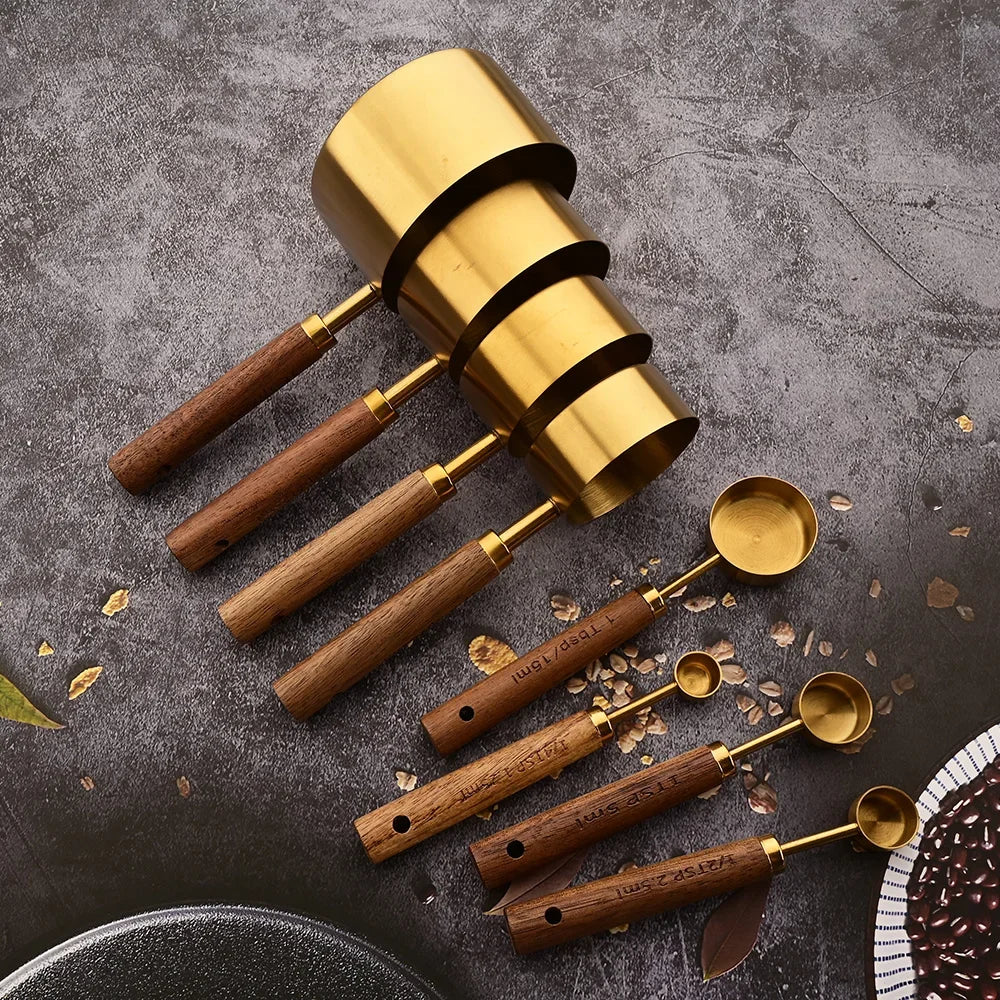 A set of stainless steel measuring spoons with wooden handles scattered on a dark gray surface.