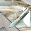 A roll of teal and gold marble self-adhesive contact paper displayed on a glass countertop.