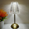 A clear glass lampshade with decorative accents sits on a brass-toned desktop reading lamp.