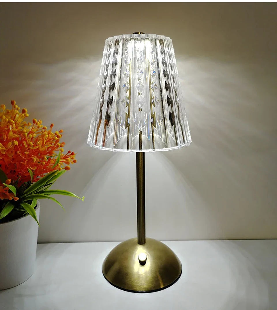 A clear glass lampshade with decorative accents sits on a brass-toned desktop reading lamp.