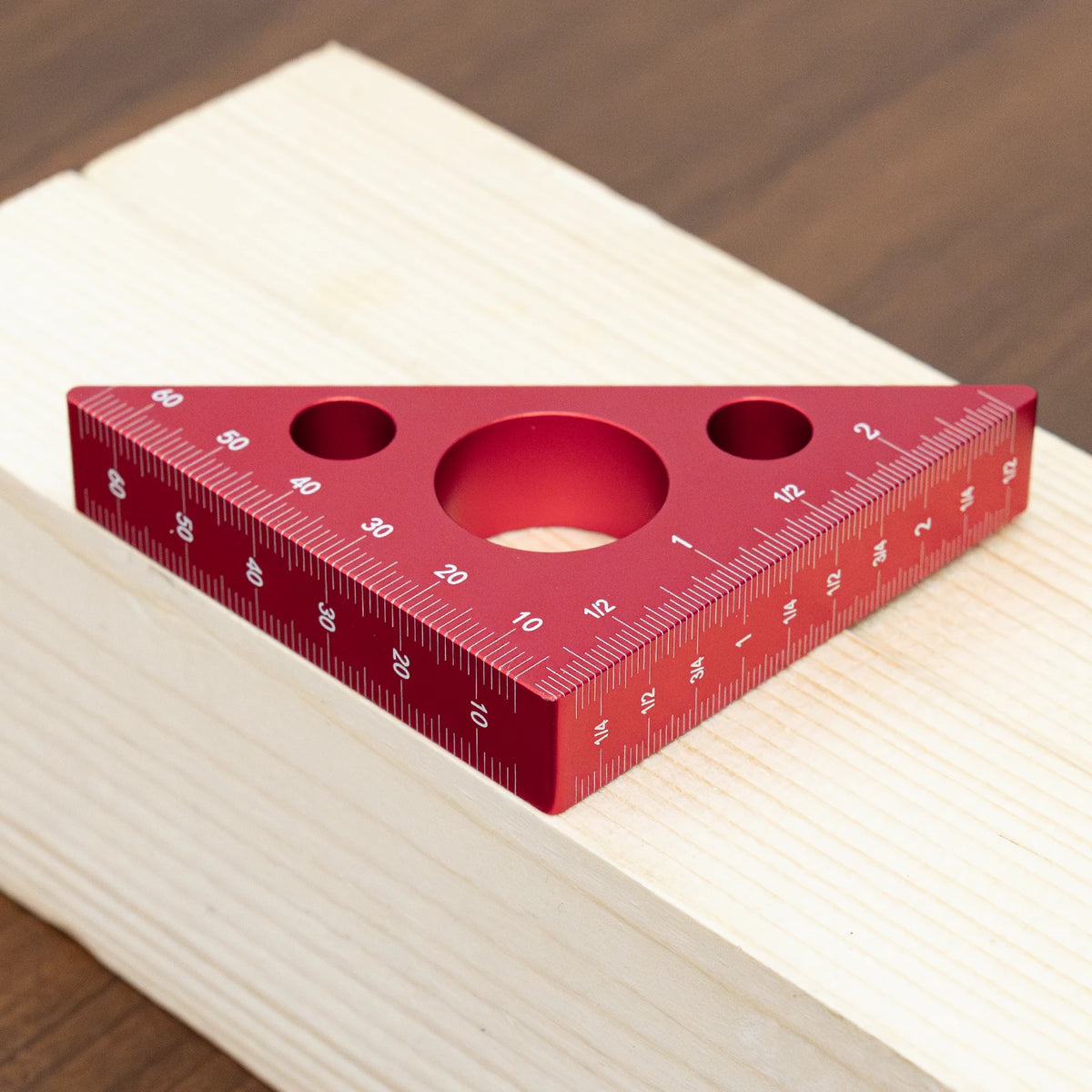 A red precision aluminum triangle ruler with imperial and metric markings resting on a light wooden surface.